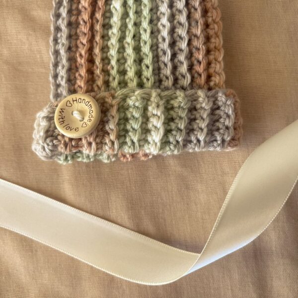 Ribbed baby beanie featuring a wooden “Handmade with love” button detail against a soft tan backdrop with cream satin ribbon.