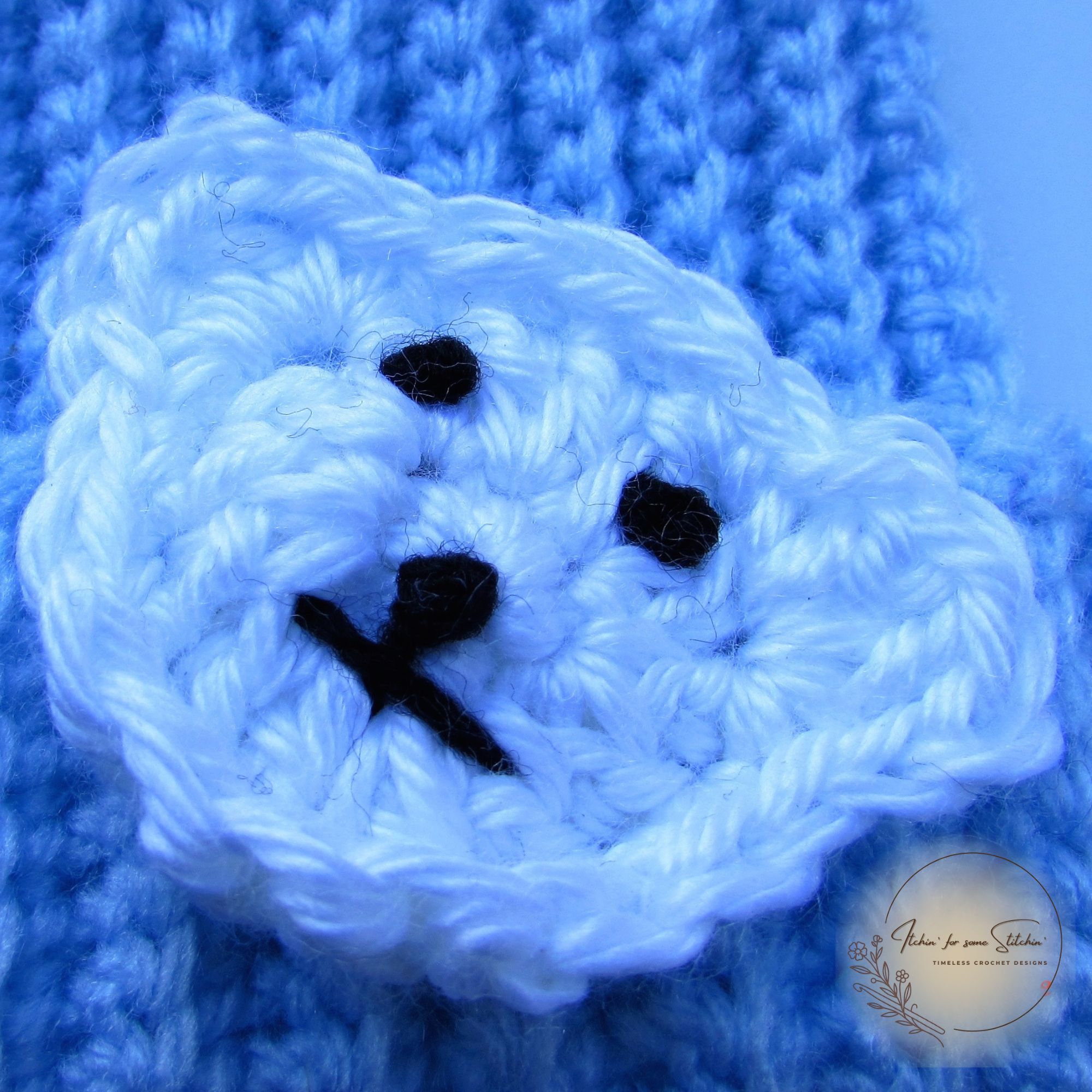 Crocheted white polar bear face appliqué attached to a light blue ribbed baby beanie, included as a bonus in the crochet pattern PDF.