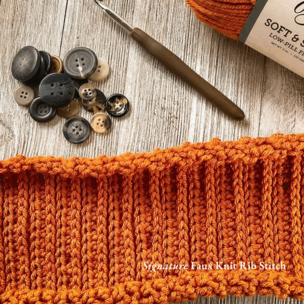 Close-up of a crochet swatch in vibrant orange yarn using the faux knit rib stitch, also known as the camel stitch. Surrounded by vintage-style buttons, a wooden-handled crochet hook, and Yarn Bee Soft & Sleek yarn on a rustic wood background. Text overlay reads “Signature Faux Knit Rib Stitch.”
