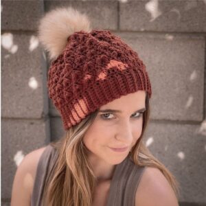 Woman wearing a deep red crochet beanie with textured leaf pattern, standing outdoors with soft background lights. Product photo for Itchin’ for Some Stitchin’ crochet pattern shop.