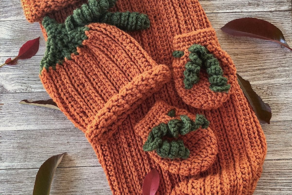 Easy crochet pumpkin baby set including cocoon sack, hat, and mittens styled with autumn leaves on a wood background in a modern vintage French Chic aesthetic.