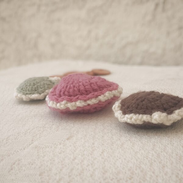 Three crochet puffed heart keepsakes in green, pink, and brown with cream edging, displayed at an angle for a close up view of edging on lace fabric.