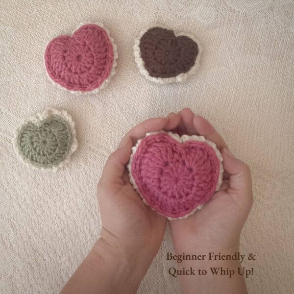 Hands gently holding a pink crochet puffed heart with cream edging. Three additional crochet hearts in pink, sage green, and brown rest on a textured cream fabric background. Text overlay reads: ‘Beginner Friendly and Quick to Whip Up!