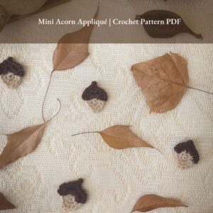 Flat lay of crocheted mini acorn appliqués on a lace background with autumn leaves. Text overlay reads: Mini Acorn Appliqué | Crochet Pattern PDF